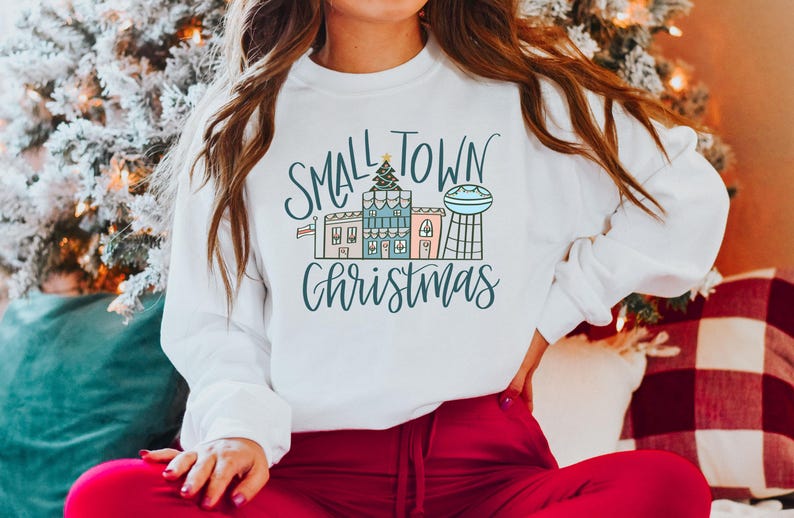 May include: White sweatshirt with a graphic design of a small town with houses and a water tower. The text "Small Town Christmas" is written in a cursive font.