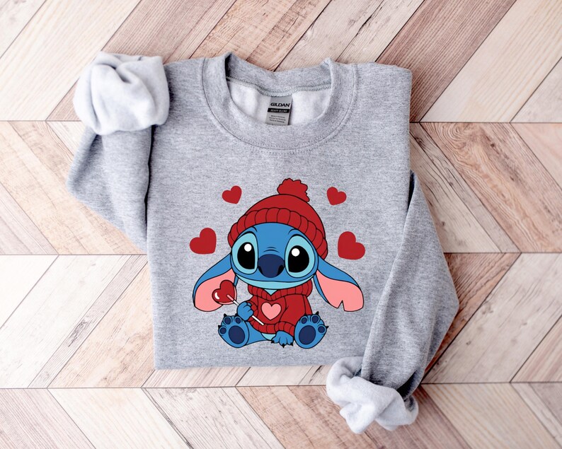 Pu&ograve; includere: Una felpa grigia con un personaggio dei cartoni animati con un cappello e un maglione rossi, che tiene in mano un lecca-lecca a forma di cuore. Il personaggio &egrave; blu con grandi occhi e orecchie rosa. Cuori rossi sparsi.