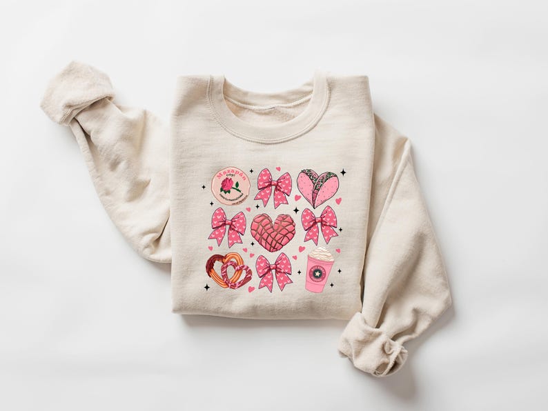 May include: A beige sweatshirt with a pink and brown graphic print of hearts, bows, and Mexican pastries. The text "La Gordita" is printed on the sweatshirt.