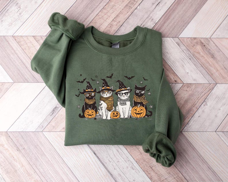 May include: Green sweatshirt with a graphic of four cats wearing witch hats and holding pumpkins. The cats are wearing glasses and have different colored fur.