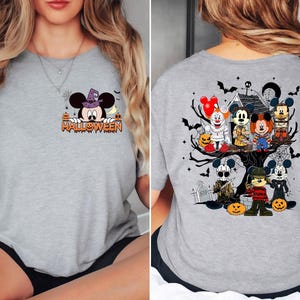 May include: Gray t-shirt with a Halloween themed design. The front of the shirt features Mickey Mouse wearing a witch hat and the text "HALLOWEEN". The back of the shirt features Mickey Mouse and friends in a spooky setting with a haunted house and a graveyard.