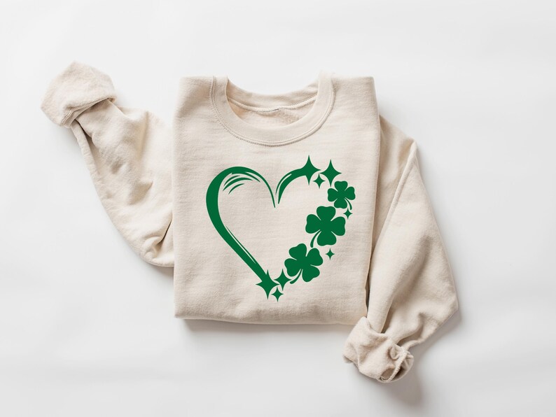 May include: A beige sweatshirt with a green shamrock heart design. The heart is outlined in green and filled with shamrocks.