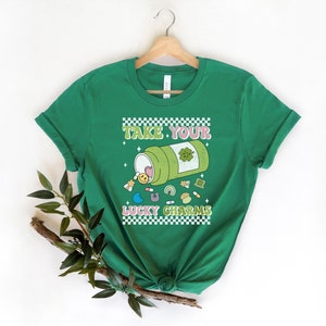 May include: Green t-shirt with a white checkered border and the text "Take Your Lucky Charms" in a retro font. A cartoon illustration of a pill bottle with a shamrock on it, spilling out lucky charms.