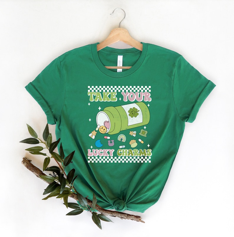 May include: Green t-shirt with a white checkered border and the text "Take Your Lucky Charms" in a retro font. A cartoon illustration of a pill bottle with a shamrock on it, spilling out lucky charms.