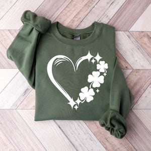 May include: A green sweatshirt with a white heart design featuring four-leaf clovers and sparkling stars.