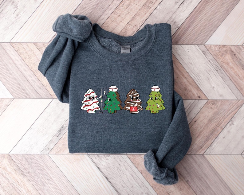 May include: A dark gray sweatshirt with a graphic of four Christmas trees dressed as nurses. The trees are wearing white nurse hats and have red crosses on their trunks.