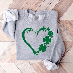 May include: A gray sweatshirt with a green shamrock heart design. The heart is outlined in green and has shamrocks and stars around it.