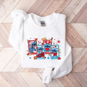 May include: White sweatshirt with a graphic print of Stitch from Lilo & Stitch. The graphic shows Stitch in four different poses with hearts and the word "LOVE".