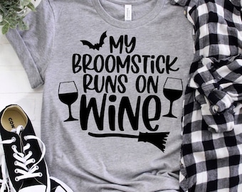 May include: A gray t-shirt with the text "My broomstick runs on wine" in black. A black bat and wine glass graphic are on the shirt. A black broom graphic is below the text.