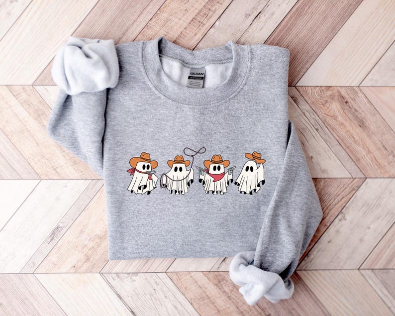May include: A heather gray sweatshirt featuring a graphic of four cartoon ghosts dressed as cowboys. Each ghost wears a cowboy hat, with bandanas and other cowboy accessories. The design is centered on the front of the sweatshirt.