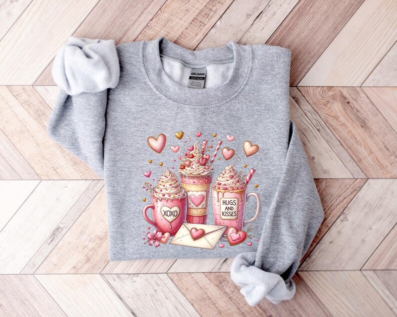 May include: Gray sweatshirt with a Valentine's Day design featuring three mugs of hot chocolate with whipped cream and hearts. The mugs have the text "XOXO", "Hugs and Kisses", and a heart.