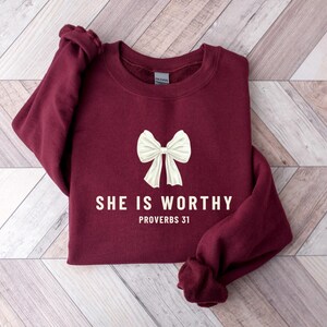 May include: Burgundy sweatshirt with a white bow and the text "She is worthy Proverbs 31" printed on the front.