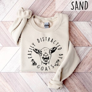 May include: A beige sweatshirt with the text "Easily Distracted By Goats" in black lettering and a goat illustration.