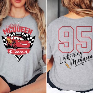 May include: Grey t-shirt with a red race car graphic and the text "Lightning McQueen Cars" on the front. The back of the shirt has the number "95" in red and the text "Lightning McQueen" in black.