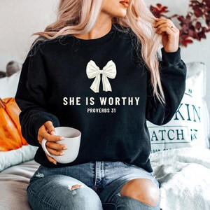 May include: A black sweatshirt with a white bow and the text "She is worthy Proverbs 31" printed on the front.