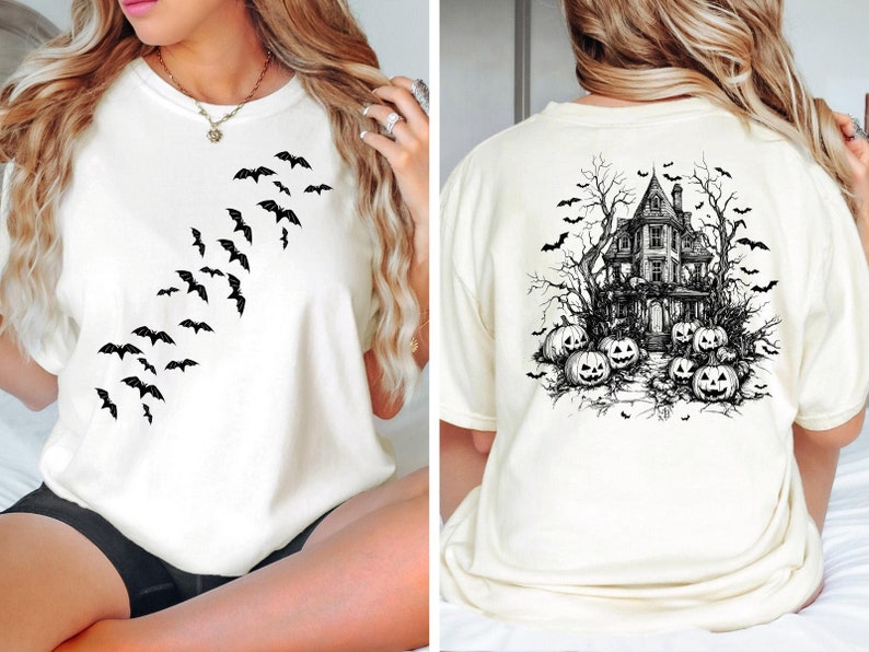 Op de afbeelding: Wit T-shirt met een zwart vleermuisontwerp aan de voorkant en een zwart-witte illustratie van een spookhuis met pompoenen aan de achterkant.