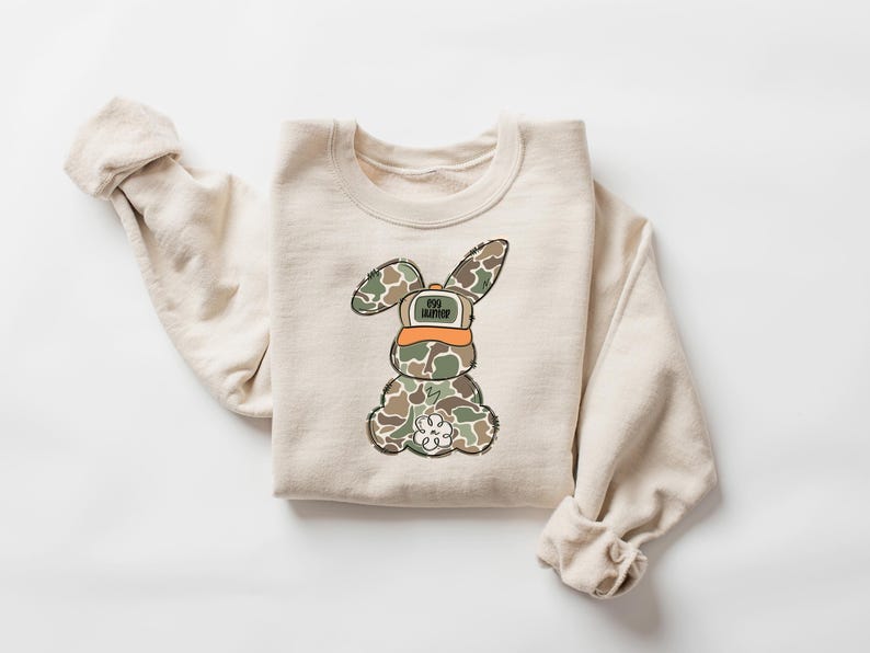 May include: A beige sweatshirt with a cartoon bunny wearing a camouflage pattern and a hat that says "Egg Hunter".