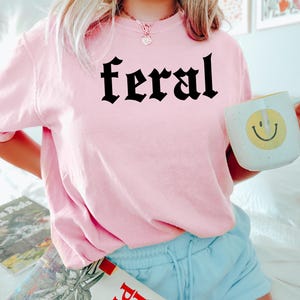 May include: A pink t-shirt with the word "feral" printed in black gothic lettering.