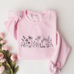 May include: A pink sweatshirt with a black line drawing of wildflowers on the front.