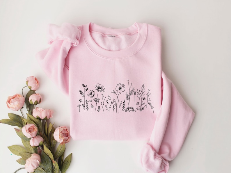 May include: A pink sweatshirt with a black line drawing of wildflowers on the front.