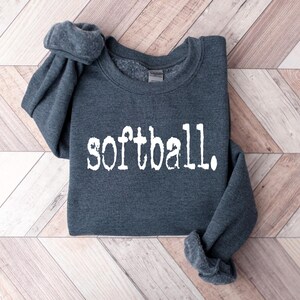 Puede incluir: Una sudadera gris oscuro con la palabra "softball" impresa en blanco en la parte delantera.
