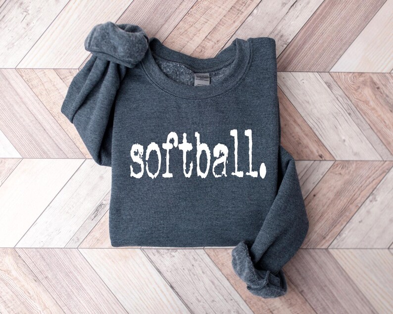Puede incluir: Una sudadera gris oscuro con la palabra "softball" impresa en blanco en la parte delantera.