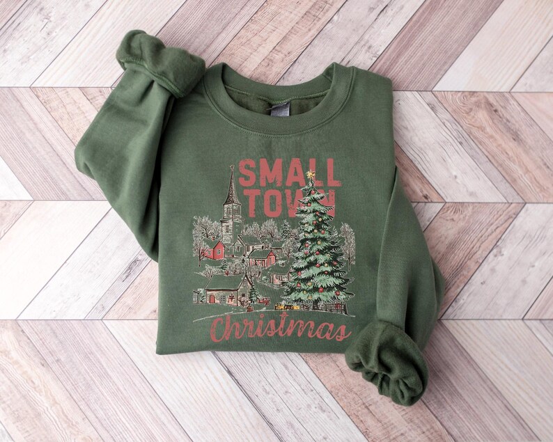 May include: Green sweatshirt with a Christmas-themed graphic that says "Small Town Christmas" and features a small town with a church and a Christmas tree.