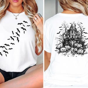 Op de afbeelding: Wit T-shirt met een zwarte afbeelding van vliegende vleermuizen aan de voorkant en een spookhuis met pompoenen aan de achterkant.