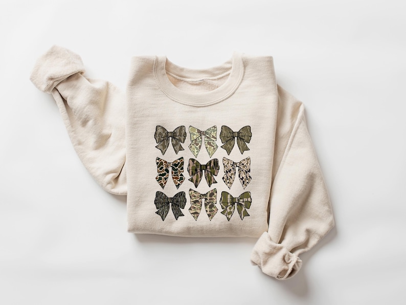 May include: A beige sweatshirt with a design of nine brown and green bows on the front.
