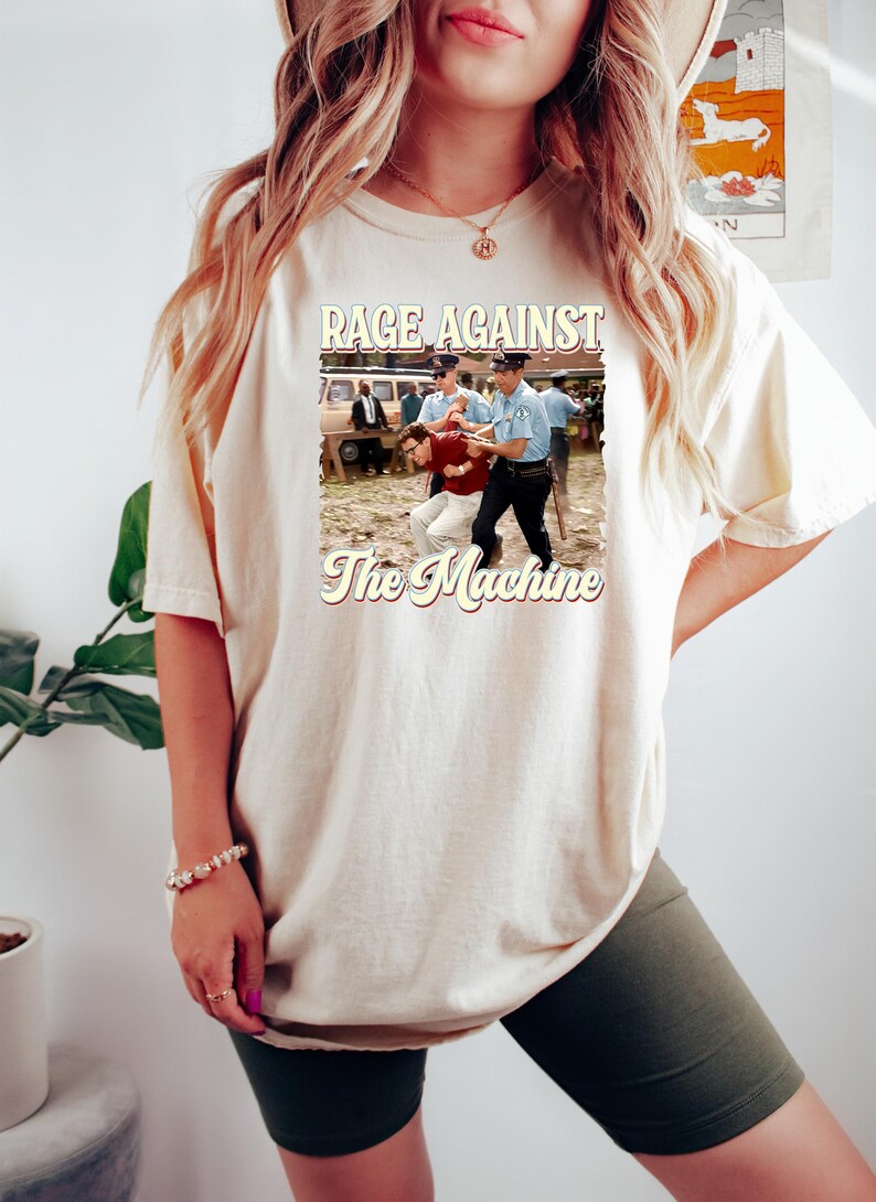 K&ouml;nnte beinhalten: Ein wei&szlig;es T-Shirt mit einer Grafik im Vintage-Stil einer Band namens "Rage Against The Machine". Die Grafik zeigt ein Schwarzwei&szlig;foto eines Mannes, der von zwei Polizisten verhaftet wird.