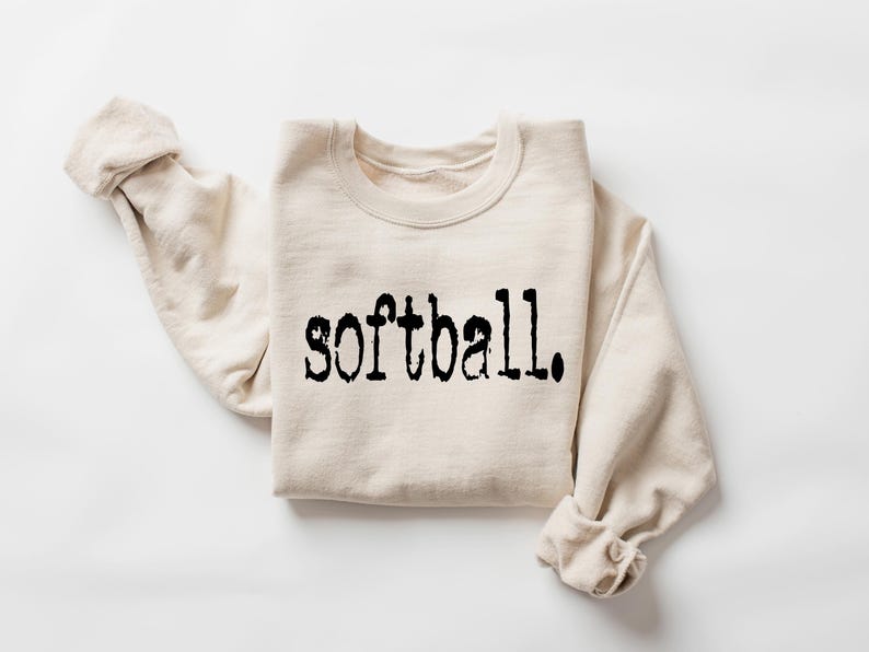 Puede incluir: Una sudadera beige con la palabra "softball" impresa en negro en la parte delantera.