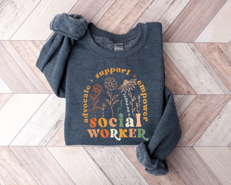May include: A dark gray sweatshirt with a floral design and the text "Support, Advocate, Empower, Social Worker" in a rainbow color scheme.