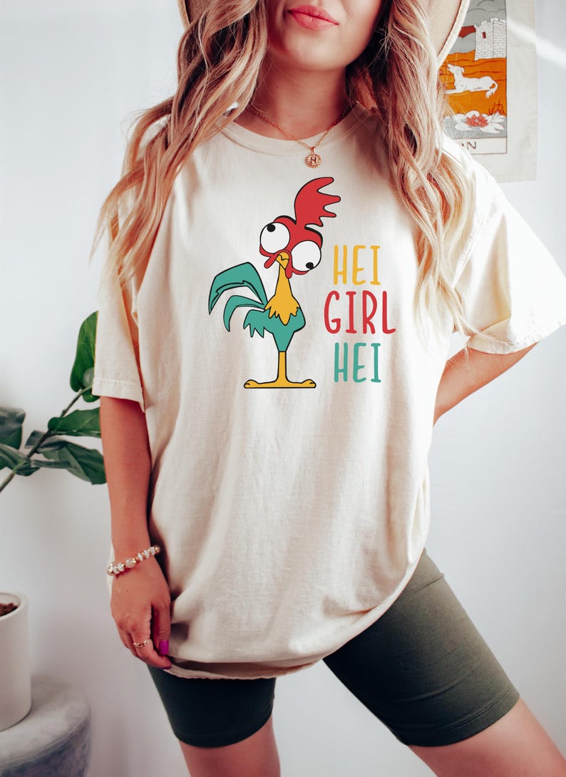 May include: A white t-shirt with a cartoon rooster wearing a red comb and a green tail. The text "Hei Girl Hei" is printed on the shirt.