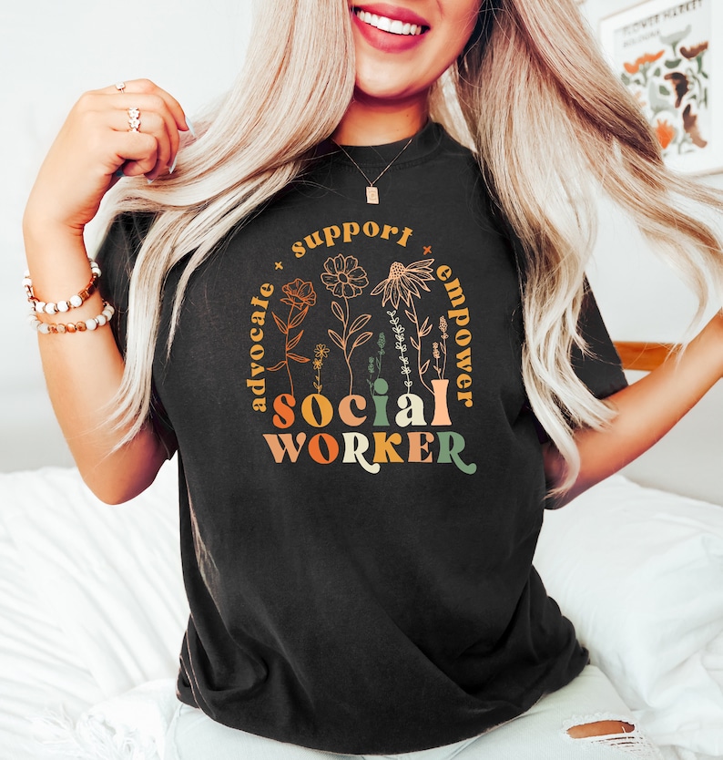 May include: Black t-shirt with a floral design and the text "support advocate social worker empower" in a rainbow color scheme.