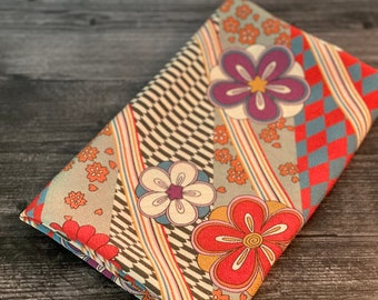 May include: A fabric with a geometric pattern of stripes, checkered squares, and stylized flowers in shades of red, orange, yellow, blue, purple, and white.