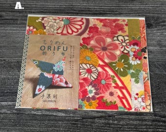 Puede incluir: Un paquete cuadrado de hojas de tela estampadas con diseños florales en rojo, rosa, amarillo y verde. Una tarjeta está adherida al frente con el texto ORIFU, SHURIKEN y caracteres japoneses, mostrando una imagen de una estrella shuriken de tela.