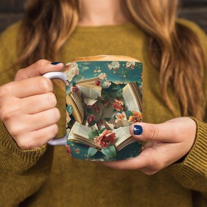 K&ouml;nnte beinhalten: Eine wei&szlig;e Keramiktasse mit einem Blumendesign, das einen Strau&szlig; aus rosa und roten Rosen und gr&uuml;nen Bl&auml;ttern zeigt. Die Tasse ist mit einer braunen Fl&uuml;ssigkeit gef&uuml;llt und hat einen Henkel auf der linken Seite. Die Tasse ist mit einem Bild von ge&ouml;ffneten B&uuml;chern verziert, deren Seiten in der Luft zu schweben scheinen.