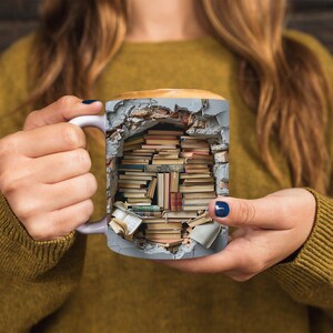 K&ouml;nnte beinhalten: Eine graue Keramiktasse mit einem Design einer Backsteinmauer, aus der B&uuml;cher herausbrechen. Die Tasse wird von den H&auml;nden einer Person gehalten.
