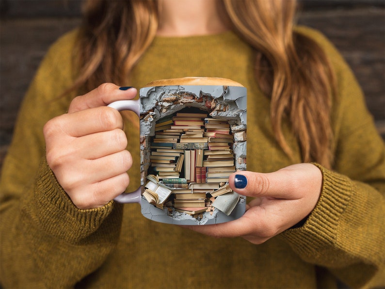 K&ouml;nnte beinhalten: Eine graue Keramiktasse mit einem Design einer Backsteinmauer, aus der B&uuml;cher herausbrechen. Die Tasse wird von den H&auml;nden einer Person gehalten.