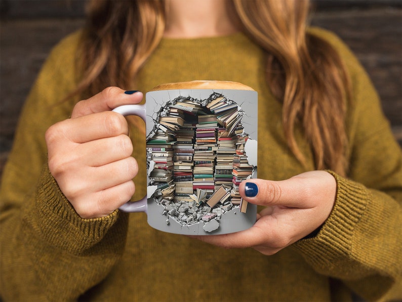 K&ouml;nnte beinhalten: Eine wei&szlig;e Keramiktasse mit einem Design einer zerbrochenen Wand, aus der B&uuml;cher herausbrechen. Die Tasse wird von den H&auml;nden einer Person gehalten.