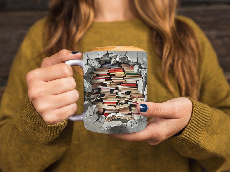 K&ouml;nnte beinhalten: Eine wei&szlig;e Keramiktasse mit einem Design aus einer zerbrochenen Backsteinmauer mit einem Stapel B&uuml;cher darin. Die Tasse wird von den H&auml;nden einer Person gehalten.