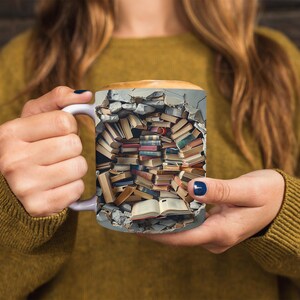 K&ouml;nnte beinhalten: Eine wei&szlig;e Keramiktasse mit einem Design einer zerbrochenen Wand, die mit gestapelten B&uuml;chern gef&uuml;llt ist. Die Tasse wird von den H&auml;nden einer Person gehalten.