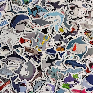 May include: A collection of colourful shark stickers with various designs and phrases. The stickers feature different shark species, including hammerhead, thresher, and great white sharks. Some stickers have humorous phrases like "I don't care for your misogyny" and "My other car is a blahaj".