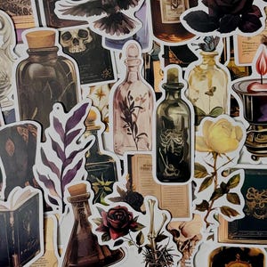 Peut inclure: Une collection d'autocollants représentant des images gothiques et mystiques, incluant des flacons de potion en verre, des crânes humains, des livres ouverts, des bougies allumées, des roses sombres, des papillons et des squelettes dans des tons de vert, or et noir.