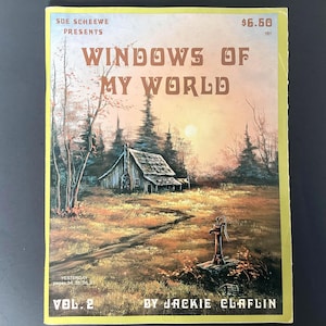 May include: A vintage book cover titled "WINDOWS OF MY WORLD" by Jackie Claflin. The cover art depicts a rustic cabin in a field with a water pump, trees, and a sunset. The book is Vol. 2 and presented by Sue Scheewe.