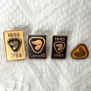 May include: A collection of vintage pins featuring a bear design. The pins are in various shapes, including rectangular and triangular, and colors, such as gold, black, and brown. The year "1885" and "Canada" are visible on some pins.