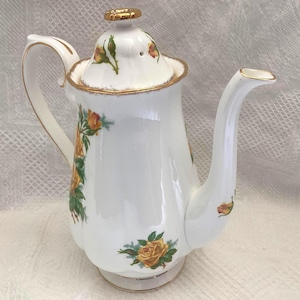 May include: White porcelain coffee pot with a gold rim and handle, adorned with yellow and orange rose floral patterns. The lid is topped with a gold accent. A classic design for serving coffee or tea.