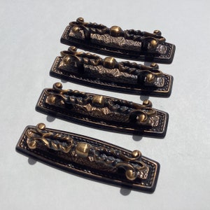 May include: Four ornate, antique-style drawer pulls with a black and gold finish. Each pull features a decorative, swirling design and a round knob.