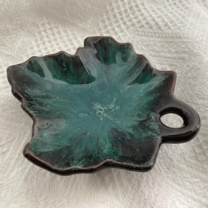 May include: A green and brown ceramic leaf-shaped dish with a handle. The dish has a marbled glaze with swirls of green and brown.