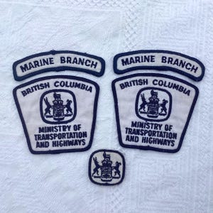 May include: A set of vintage Marine Branch patches from British Columbia. The patches are white with black text and borders. The text includes "MARINE BRANCH", "BRITISH COLUMBIA", and "MINISTRY OF TRANSPORTATION AND HIGHWAYS".